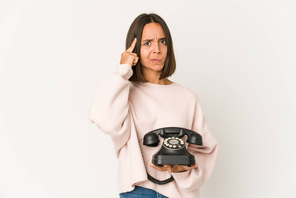 Young hispanic woman holding a vintage telephone isolated pointing temple with finger, thinking, focused on a task. - Photo, Image