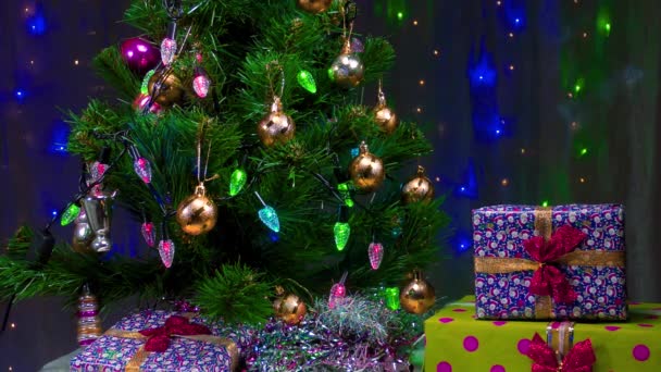 Πράσινο χριστουγεννιάτικο δέντρο και δώρα στο παρασκήνιο της αναβοσβήνει γιρλάντες - Πλάνα, βίντεο