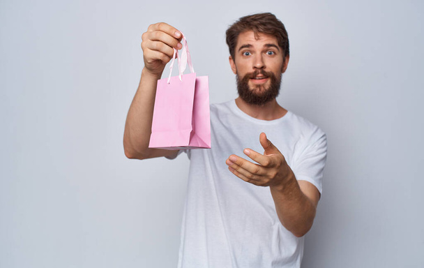 bearded man in white t-shirt holding pink gift bag in hands isolated background - Фото, зображення