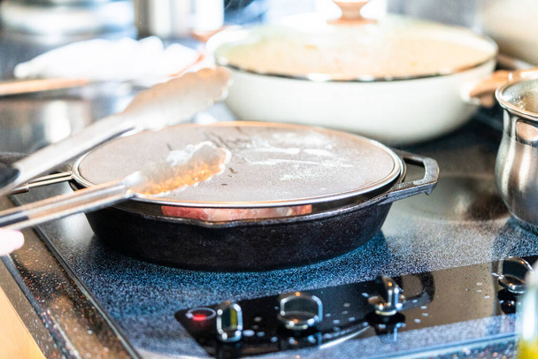 Τηγανίζοντας την μπριζόλα της Νέας Υόρκης σε τηγάνι από χυτοσίδηρο πάνω από την ηλεκτρική κουζίνα. - Φωτογραφία, εικόνα