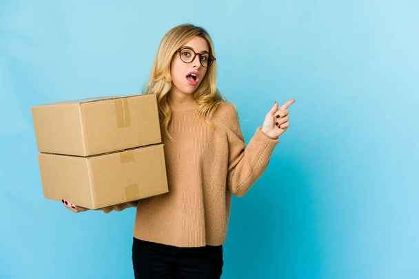 Mladá blondýnka běloška žena drží krabice přesunout ukazující na stranu - Fotografie, Obrázek