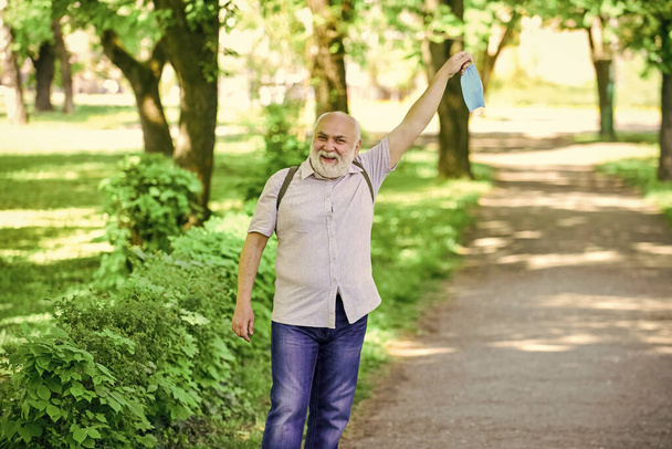 old man walking in park. life during coronavirus lockdown. enjoy the beauty. fear of illness. strategy in battling virus. prohibition on visiting public places. senior man take off medical mask - Фото, изображение
