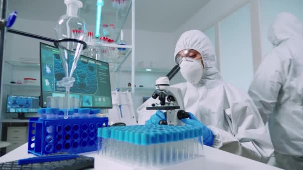Suojapukuinen tutkija, joka analysoi viruksia mikroskoopilla - Materiaali, video