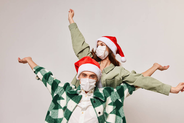 happy man in plaid shirt and woman in festive hat gesturing with hands, medical mask on face - 写真・画像