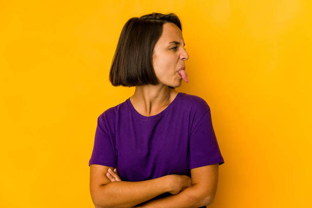 Jeune femme hispanique isolée sur jaune drôle et amical collant sur la langue. - Photo, image