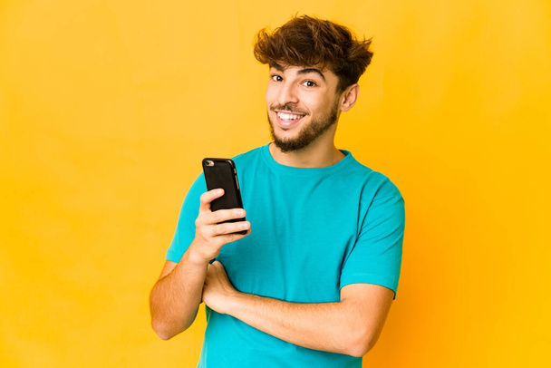 Young indian man holding a phone laughing and having fun. - 写真・画像