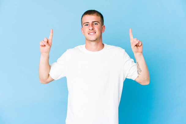 Jovem caucasiano bonito homem indica com ambos os dedos dianteiros para cima mostrando um espaço em branco. - Foto, Imagem