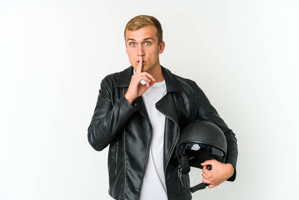 Joven hombre caucásico sosteniendo un casco de moto aislado sobre fondo blanco manteniendo un secreto o pidiendo silencio. - Foto, imagen