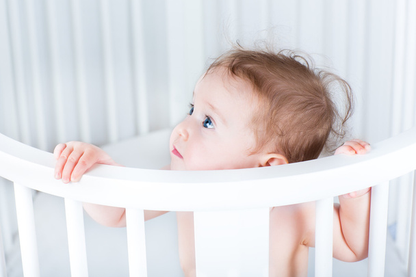 little baby standing in a round white crib - Photo, Image