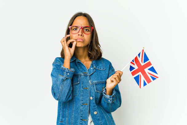 Fiatal latin nő kezében egy angol zászló elszigetelt fehér háttér ujjaival ajkain tartja a titkot. - Fotó, kép