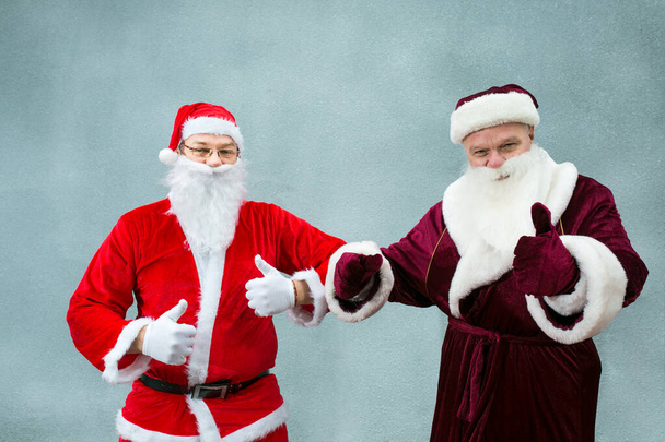 Rusya 'dan Ded Moroz ve Noel Baba tanıştı. Noel Baba 'nın ellerinde "Tamam" işareti var. Gri arkaplanda yakın plan. - Fotoğraf, Görsel