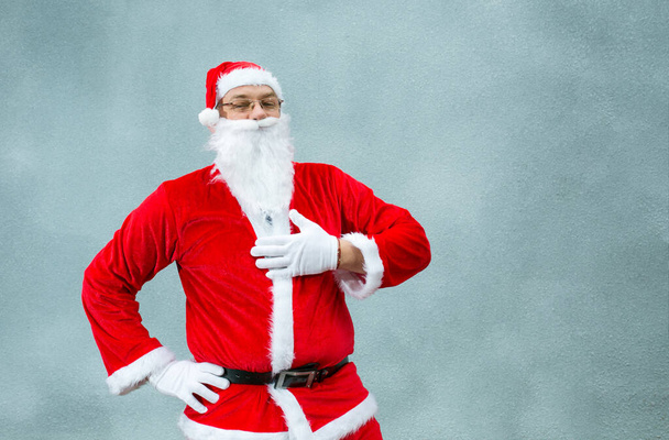 Weihnachtsmann in Großaufnahme auf grauem Hintergrund. Weihnachtsmann streicht sich über den Bart. - Foto, Bild