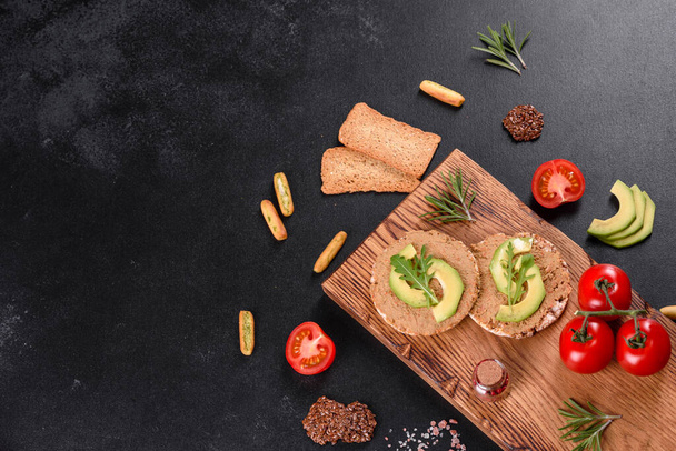 Νόστιμο φρέσκο σάντουιτς με πάστα ήπατος, κομμάτια αβοκάντο και ρόκα σε σκουρόχρωμο τραπέζι τσιμέντου - Φωτογραφία, εικόνα