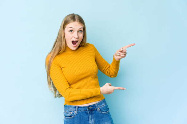 Young blonde woman isolated on blue background excited pointing with forefingers away. - Photo, Image