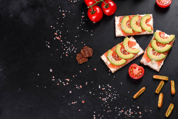Heerlijk vers broodje met rode vis, boter, brood en avocado op een donkere betonnen tafel - Foto, afbeelding