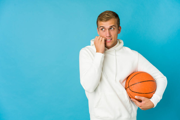 Jonge blanke man basketbal geïsoleerd op blauwe achtergrond ontspannen denken over iets op zoek naar een kopieerruimte. - Foto, afbeelding