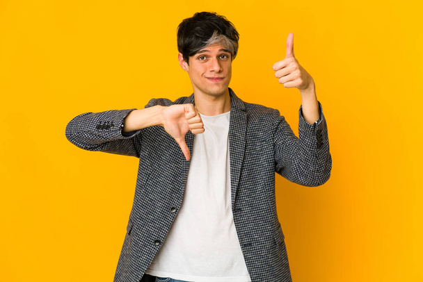 Молодий худий іспаномовний чоловік показує великі пальці вгору і великі пальці вниз, важко вибрати концепцію
 - Фото, зображення
