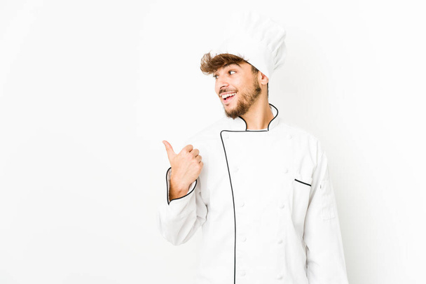Joven cocinero árabe señala con el dedo pulgar de distancia, riendo y sin preocupaciones. - Foto, imagen