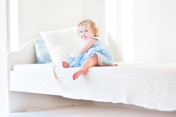Pikkutyttö istuu valkoisella sängyllä
 - Valokuva, kuva