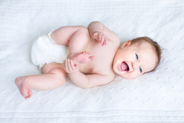 Bebé riéndose usando un pañal jugando con sus pies
 - Foto, imagen