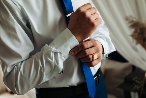 A sexy male businessman fastens a cufflink on his wrist watch, the cuff of the sleeve of a luxurious white shirt. Tonal correction - Фото, зображення