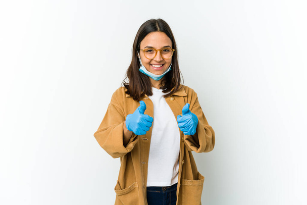 Young latin woman wearing a mask to protect from covid isolated on white background with thumbs ups, cheers about something, support and respect concept. - Photo, Image