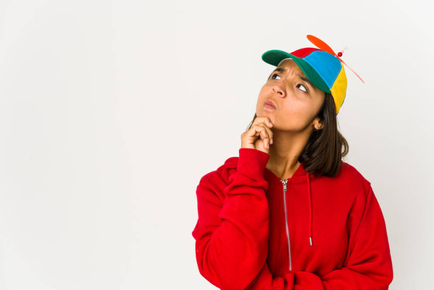 Young hispanic woman wearing a cap with propeller isolated looking sideways with doubtful and skeptical expression. - Photo, Image