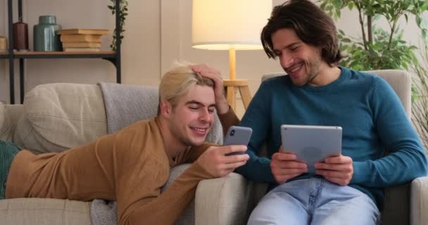 Gay couple using mobile phone and digital tablet at home - Záběry, video
