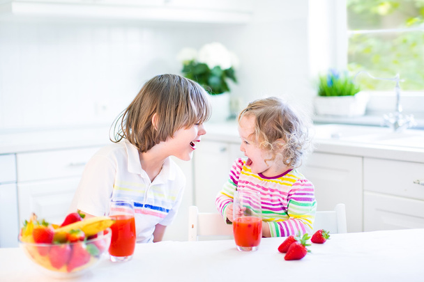 Happy teenager boy and his cute toddler sister having fruit for breakfast - Foto, afbeelding