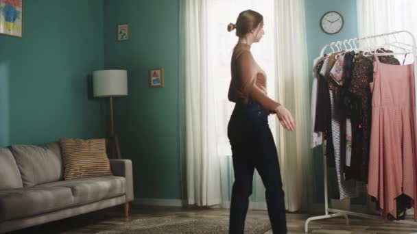 Tyttö huoneessa hajottaa vaatteita ripustimesta - Materiaali, video