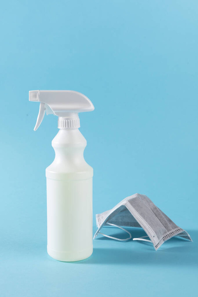 A vertical shot of a sanitizing spray and a surgical mask on a blue surface - Foto, imagen