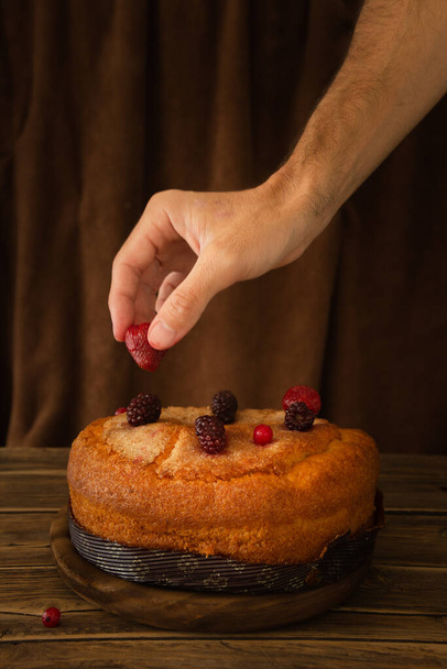 A vertical shot of a hand putting strawberry on a delicious sponge cake - Фото, зображення