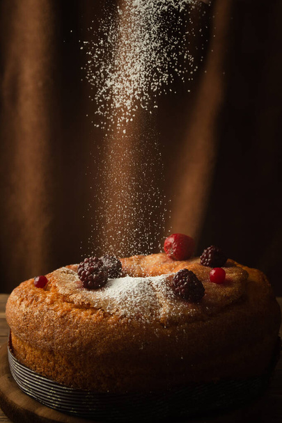 A vertical shot of a delicious cake with powdered sugar, red berries, strawberries, and blackberries - Fotografie, Obrázek