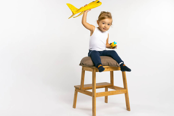 A little girl is sitting on a large stool with a yellow plane in her hands and posing. The concept of gender stereotypes. High quality photo - Foto, Imagem