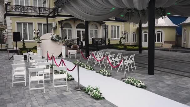 Das Restaurant ist mit einem weißen Gehweg und Stühlen dekoriert, ein runder Fotobereich mit frischen Blumenarrangements für eine Hochzeitszeremonie unter freiem Himmel - Filmmaterial, Video