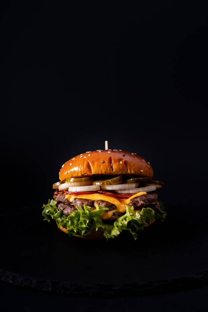 A vertical shot of a delicious burger on a black surface - Foto, Bild