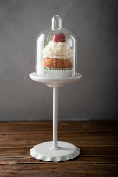 A vertical shot of a delicious cupcake with cream and cherry on top on a dessert stand - Foto, afbeelding