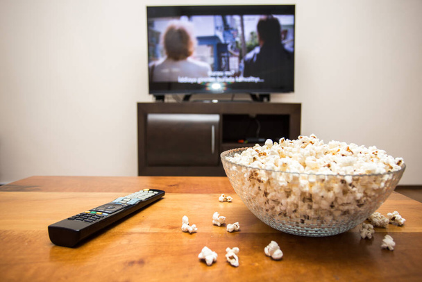 Tv remote control and popcorn on a wooden brown coffee table. Concept of stay home in the pandemic. - Foto, imagen