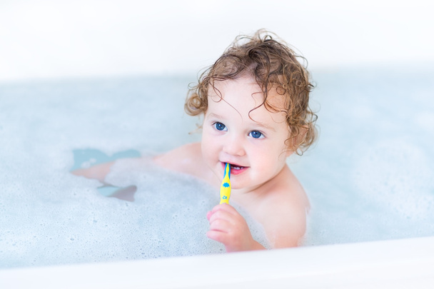 Дитина з красивими блакитними очима і кучеряве волосся приймає ванну
 - Фото, зображення