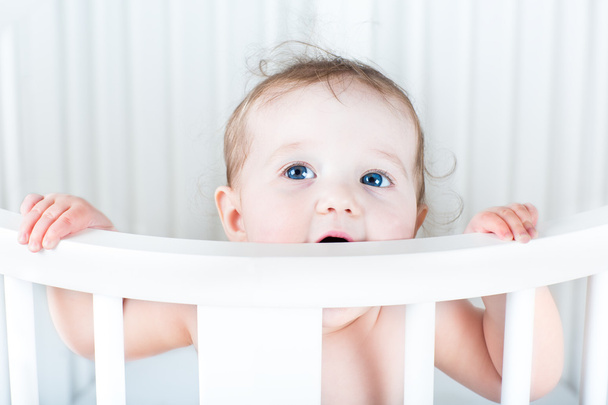 little baby standing in a round white crib - Fotó, kép