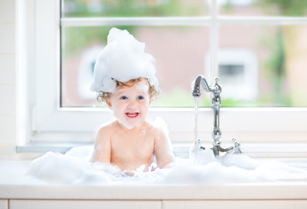 Baby girl with big blue eyes playing in a bath - Photo, Image