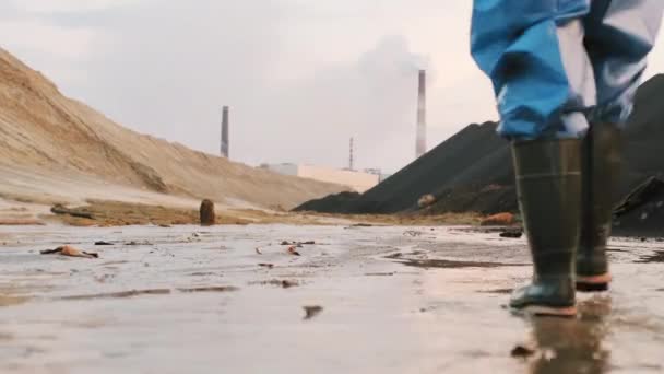 品質管理のための汚染された町の郊外保持装置の泥だらけの領域を歩く保護スーツやゴムブーツで2人の生態学者のバックビューショット - 映像、動画