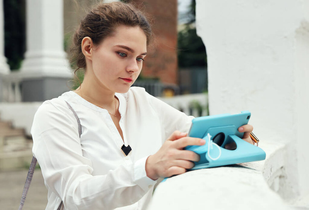 Jovem mulher de blusa branca olha atentamente para a tela do tablet em suas mãos no dia de verão - Foto, Imagem