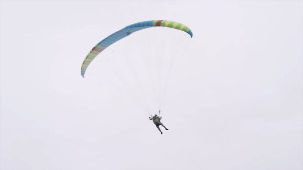 Vue arrière d'un parachutiste tournant en l'air avec un parachute d'aile. L'action. parachutiste professionnel tirant la fronde pour contrôler le parachute tout en volant sur fond gris ciel nuageux. - Photo, image