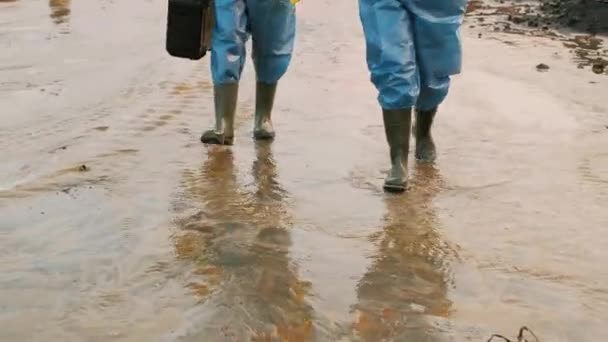 Naklápěcí záběry dvou ekologek ve speciálních ochranných oblecích a respiračních maskách kontrolujících současnou ekologickou situaci v nejvíce znečištěné oblasti procházejících bahnem - Záběry, video