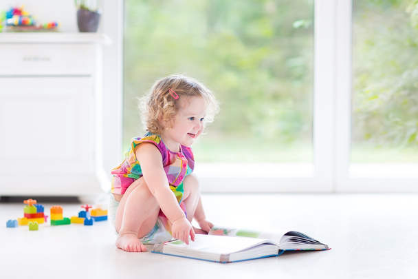 Toddler girl reading a book sitting on a floor - Photo, Image