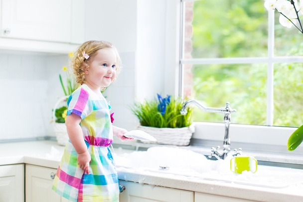 κορίτσι πλύσιμο των πιάτων, καθαρισμός με ένα σφουγγάρι και να παίζει με αφρό - Φωτογραφία, εικόνα