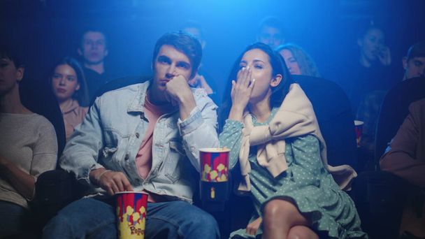 Сонная женщина зевает в кино. Уставшая пара смотрит фильм в кинотеатре. - Фото, изображение