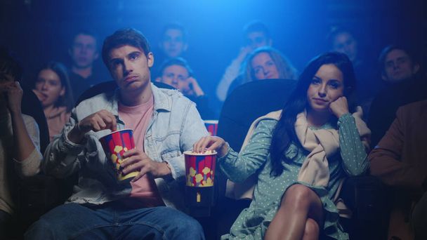 Upset couple eating popcorn in movie theater. Friends watching film in cinema. - Foto, Imagen