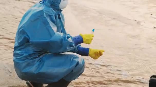 Foto de seguimiento medio de dos ambientalistas en trajes de protección especiales, guantes y máscaras que prueban el agua contaminada en el control de calidad en una de las áreas más tóxicas y peligrosas - Metraje, vídeo